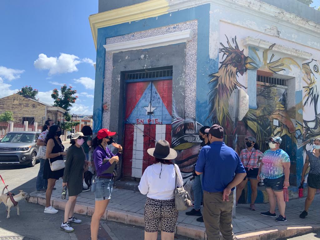 Personas esperan frente a esquina con arte callejero en Ponce.